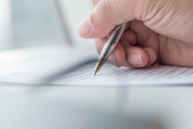 a person writing on a piece of paper with a pen.